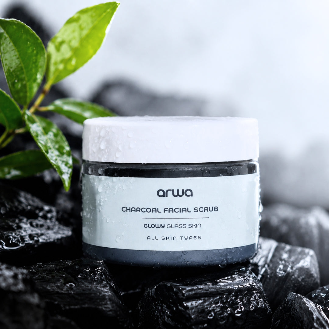 Jar of Arwa Charcoal Facial Scrub on a dark surface with green leaves in the background